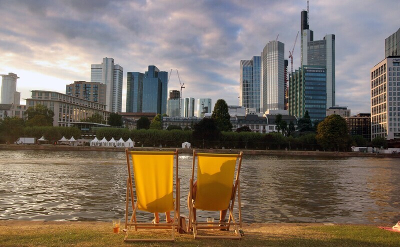 Blick auf die Frankfurter Skyline vom Mainufer: Liegestuhl statt Büro? Ganz so bequem ist mobiles Arbeiten nicht. Für Angestellte und Vorgesetzte von Banken hat es dennoch viele Vorteile. | © Imago / Ralph Peters