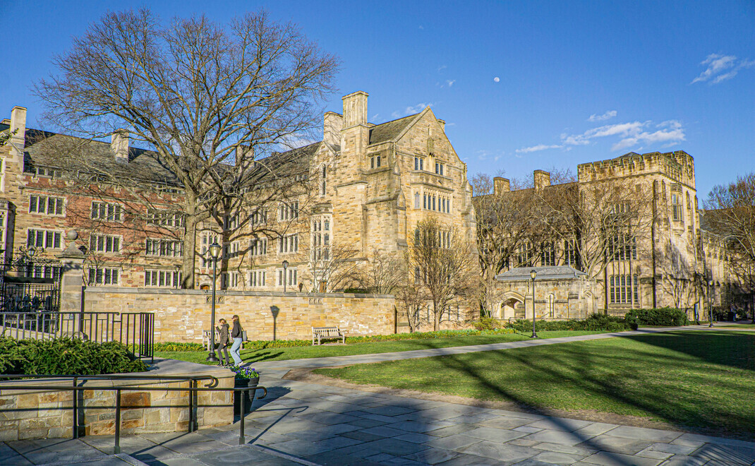 Sonniger Winterblick auf den historischen Campus der Yale University mit gotischen Sandsteingebäuden, kahlen Bäumen und vereinzelten Studierenden auf gepflasterten Wegen vor blauem Himmel.